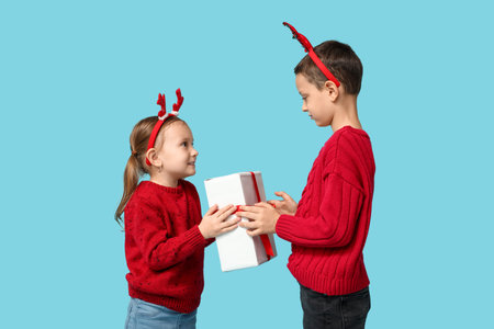 Cute little children in reindeer horns with Christmas gift on blue backgroundの写真素材
