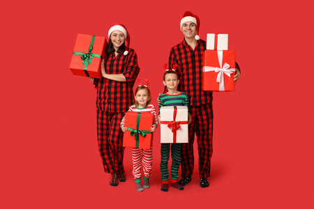 Happy family in pajamas with Christmas gifts on red backgroundの写真素材