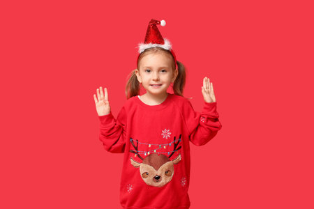 Cute little girl in Christmas sweater on red backgroundの写真素材