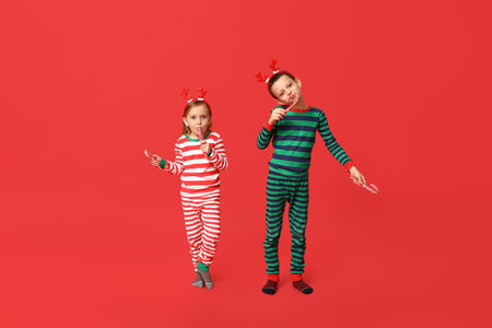 Cute little children in pajamas with candy canes on red backgroundの写真素材
