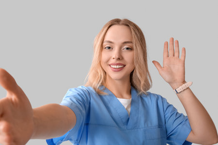 Beautiful female doctor waving hand and reaching out for handshake on gray backgroundの写真素材
