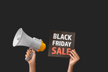 Female hands holding poster with text BLACK FRIDAY SALE and megaphone on dark backgroundの写真素材