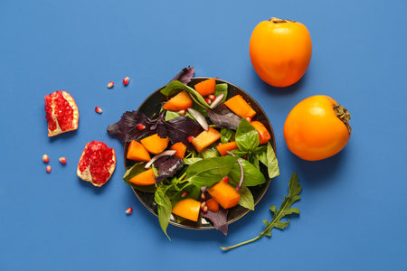 Plate of delicious salad with persimmon, pomegranate seeds and onion on blue backgroundの写真素材