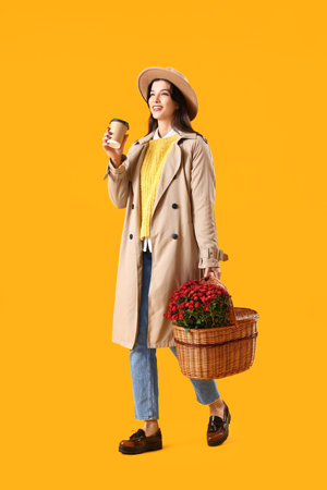 Stylish young woman with chrysanthemum flowers and coffee cup on yellow backgroundの写真素材