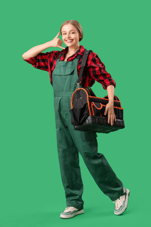 Female worker with bag of tools showing "call me" gesture on green backgroundの写真素材