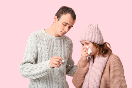 Young man with thermometer and his ill girlfriend on pink backgroundの写真素材