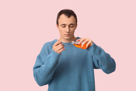 Ill young man taking cough syrup on pink background