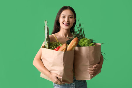Young Asian woman with shopping bags full of fresh food on green backgroundの写真素材