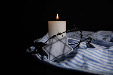 Burning candle with barbed wire, Jewish badge and prisoner uniform on dark background. International...
