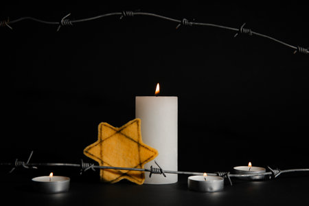 Burning candles with Jewish badge and barbed wire on dark background. International Holocaust Remembrance Dayの写真素材