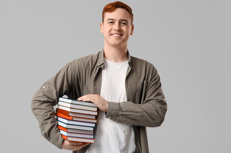 Smiling young man with stack of different books on gray backgroundの写真素材
