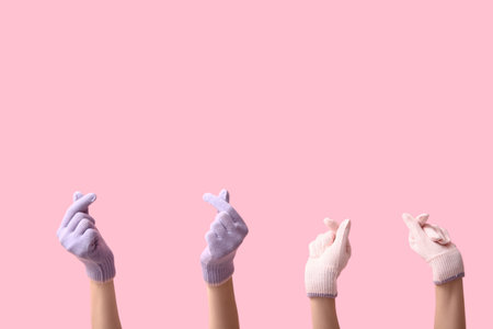 Women in warm gloves showing hearts on pink backgroundの写真素材