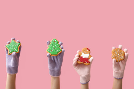 Female hands in warm gloves with tasty Christmas cookies on pink backgroundの写真素材