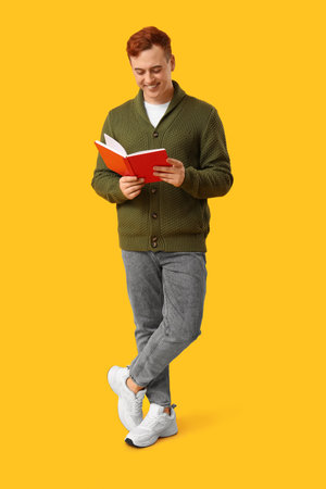 Smiling man reading book on yellow backgroundの写真素材