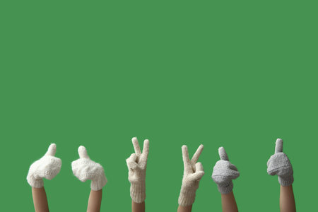 Women in warm mittens showing thumb-up and victory gesture on green backgroundの写真素材