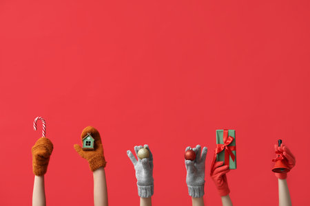 Female hands in warm gloves with Christmas decorations and gift box on red backgroundの写真素材