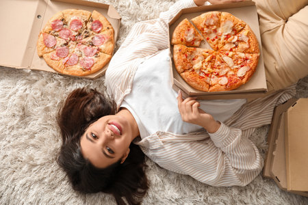 Young woman with cardboard boxes of tasty pizzas on carpet at homeの写真素材