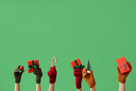 Female hands in warm mittens with Christmas gifts and decorations on green backgroundの写真素材