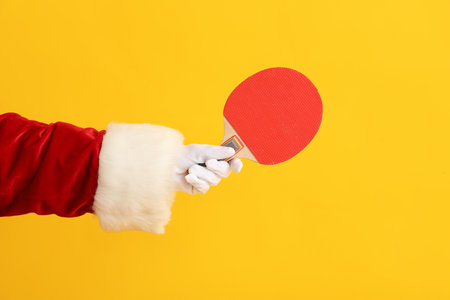 Santa Claus hand with ping-pong racket on yellow background, closeupの写真素材