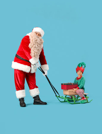 Santa Claus and cute little elf with Christmas gifts sledding on blue backgroundの写真素材
