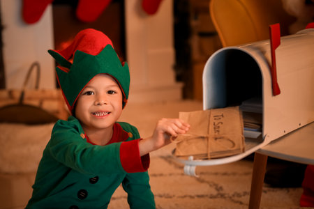 Cute little elf putting letters to Santa Claus in mail box at home on Christmas Eveの写真素材