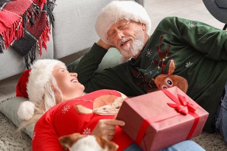 Happy mature couple with dog and gift lying at home on Christmas Eveの写真素材