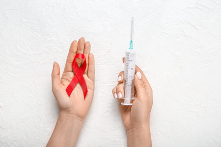 Female hands with red ribbon and syringe on white grunge background. AIDS Day concept