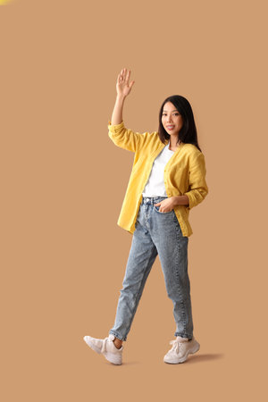 Beautiful young Asian woman waving hand on beige backgroundの写真素材