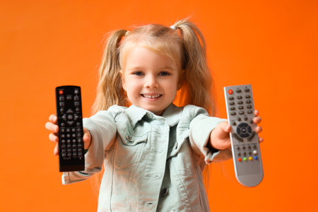 Little girl with TV remote controls on orange backgroundの写真素材