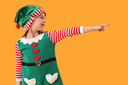 Cute little girl in elf's costume pointing at something on yellow backgroundの写真素材