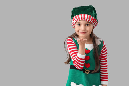 Cute little girl in elf's costume blowing kiss on gray backgroundの写真素材