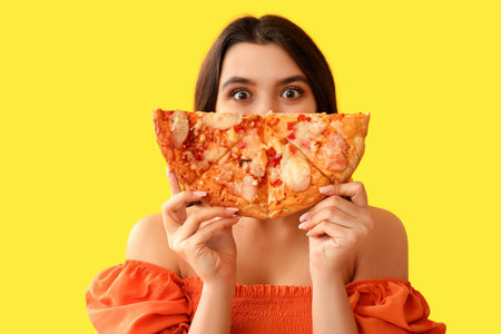 Young woman with tasty pizza on yellow backgroundの写真素材