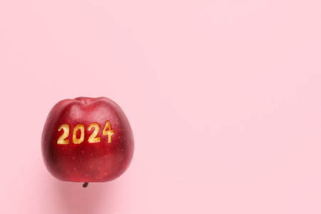Ripe apple with carved figure 2024 on pink backgroundの写真素材