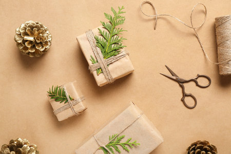 Painted golden pine cones with Christmas gift boxes and coniferous branches on beige background