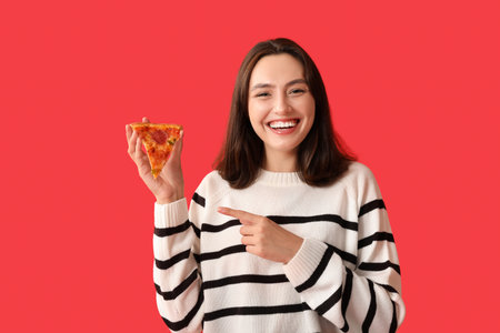 Young woman holding piece of tasty pizza on red backgroundの写真素材