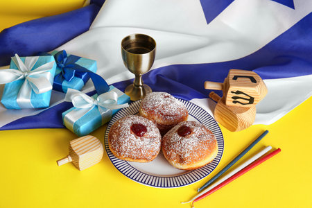 Israel flag with tasty donuts, gift boxes, dreidels and cup on yellow background. Hanukkah celebrationの写真素材
