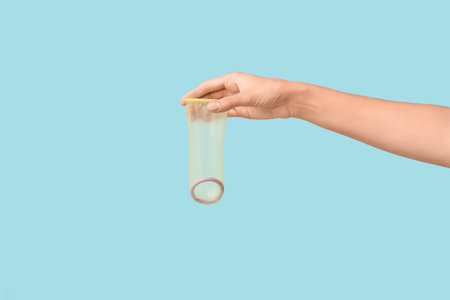 Female hand with open condom on blue background. Safe sex conceptの写真素材