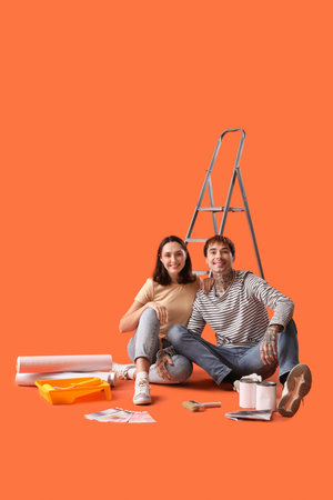 Young couple with painting tools sitting on orange backgroundの写真素材