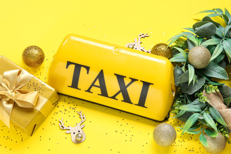 Composition with taxi roof sign, gift box and Christmas decorations on yellow backgroundの写真素材