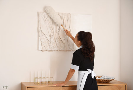 Pretty chambermaid cleaning hotel room with pp-duster