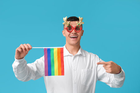 Young man in Christmas eyeglasses pointing at LGBT flag on blue backgroundの写真素材
