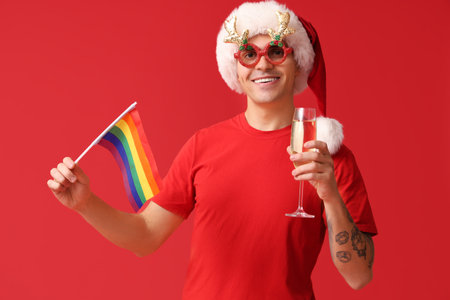 Young man in Santa hat with LGBT flag and champagne on red backgroundの写真素材