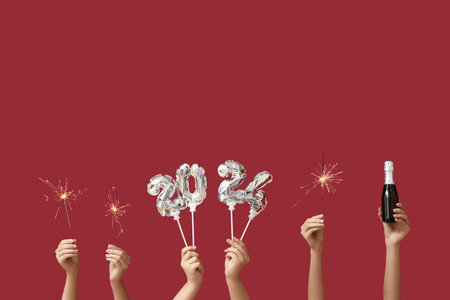 Female hands with Christmas sparklers, champagne bottle and figure 2024 made of balloons on red backgroundの写真素材