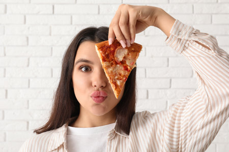 Young woman with piece of tasty pizza on white brick backgroundの写真素材