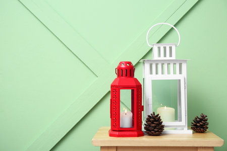 Christmas lanterns with burning candles and pine cones on wooden stool near color wallの写真素材
