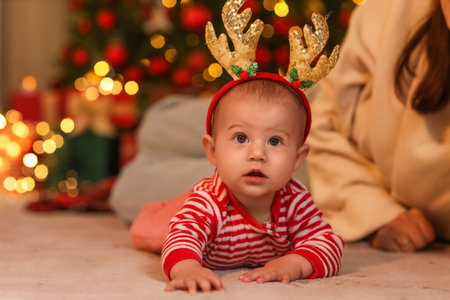 Cute little baby in reindeer horns at home on Christmas Eveの写真素材