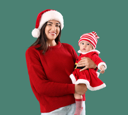 Young mother with cute little baby in Santa Claus costume on green backgroundの写真素材