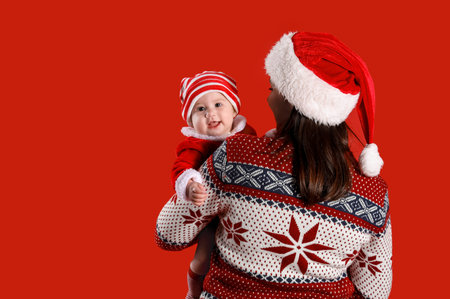 Cute little baby in Santa Claus costume with mother on red backgroundの写真素材