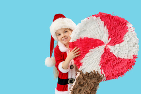 Cute little girl in Santa Claus costume with lollipop pinata on blue backgroundの写真素材