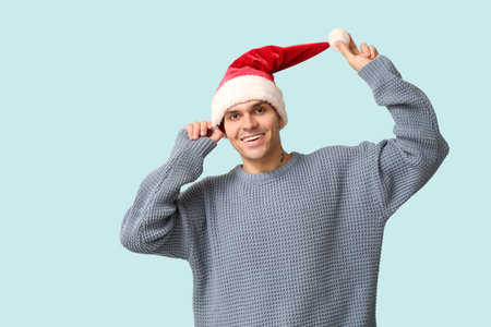 Handsome young man in Santa hat and warm sweater on blue backgroundの写真素材